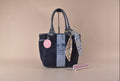 A Coach Affair tote bag in navy blue canvas with a light blue vertical stripe, gold-tone hardware, a pink circular hangtag, and a blue-and-white patterned scarf tied to the side, set against a solid beige background.